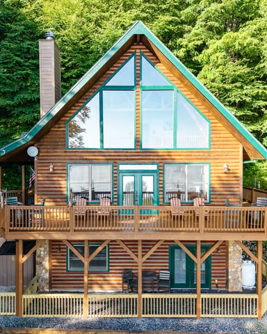 Rustic wooden cabin with metal roof nestled among tall trees on a gravel driveway